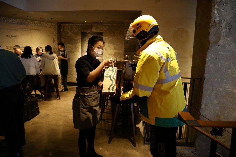 FILE PHOTO: A staff member takes a bag of ordered food from a Meituan delivery worker at a Starbucks flagship store in Beijing, China January 18, 2022. REUTERS/Tingshu Wang/File Photo