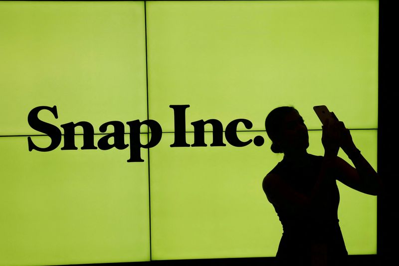 FILE PHOTO: A woman stands in front of the logo of Snap Inc. on the floor of the New York Stock Exchange while waiting for Snap Inc. to post their IPO, in New York City, NY, U.S. March 2, 2017. REUTERS/Lucas Jackson/File Photo