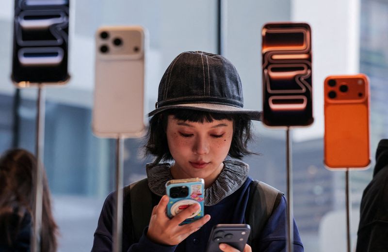 FILE PHOTO: A woman uses her smartphone inside the Apple store in Beijing's Sanlitun area as the iPhone 17 series smartphones go on sale in Beijing, China September 19, 2025. REUTERS/Maxim Shemetov/File Photo