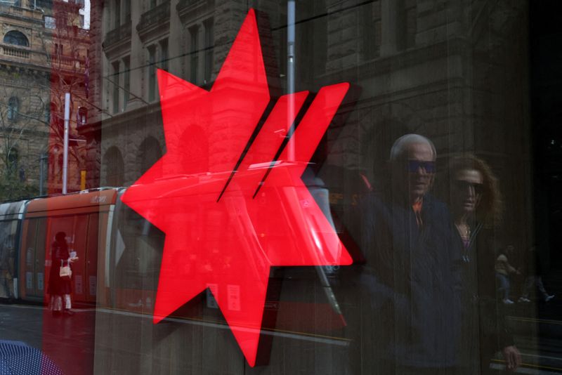 FILE PHOTO: People are reflected next to a National Australia Bank (NAB) logo displayed on panel of a NAB branch as they walk through the Central Business District (CBD) in Sydney, Australia, August 19, 2025. REUTERS/Hollie Adams/File Photo