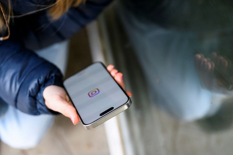 A teenager poses for a picture while looking at a phone, in Bonn, Germany, February 20, 2026. REUTERS/Jana Rodenbusch