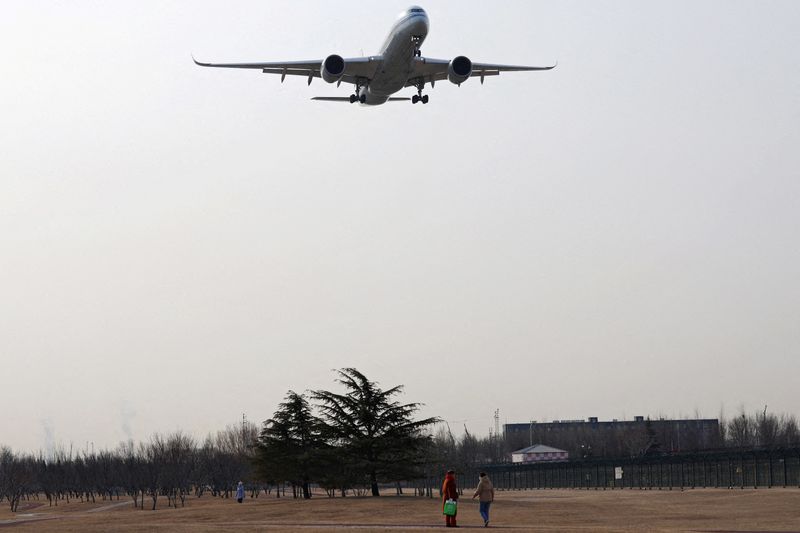 FILE PHOTO: An aircraft flies above visitors at a park near the Beijing Capital International Airport in Beijing, China February 2, 2024. REUTERS/Florence Lo/File Photo