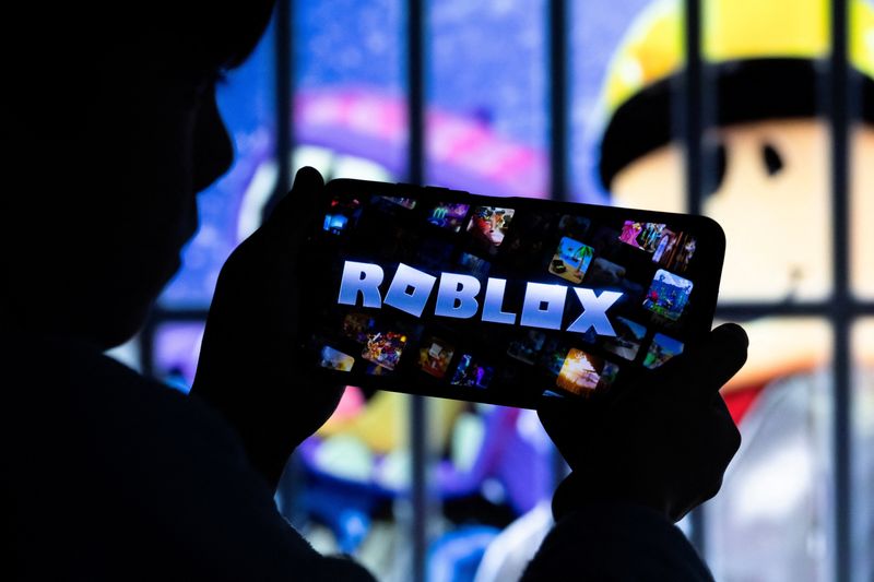 A boy poses for a photo while holding a smartphone in front of a screen displaying a character of the U.S. children's video game Roblox, in this illustration taken December 8, 2025. REUTERS/Ramil Sitdikov/Illustration