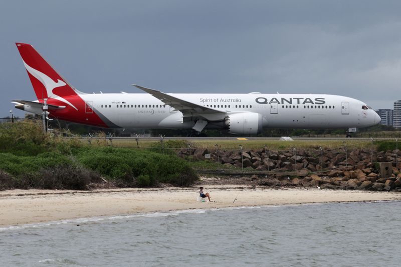 FILE PHOTO: A fisherman sits on the beach as a Qantas Dreamliner taxis along a runway at Sydney Airport on the day they announced their half-year results, in Sydney, Australia, February 26, 2026. REUTERS/Hollie Adams/File Photo