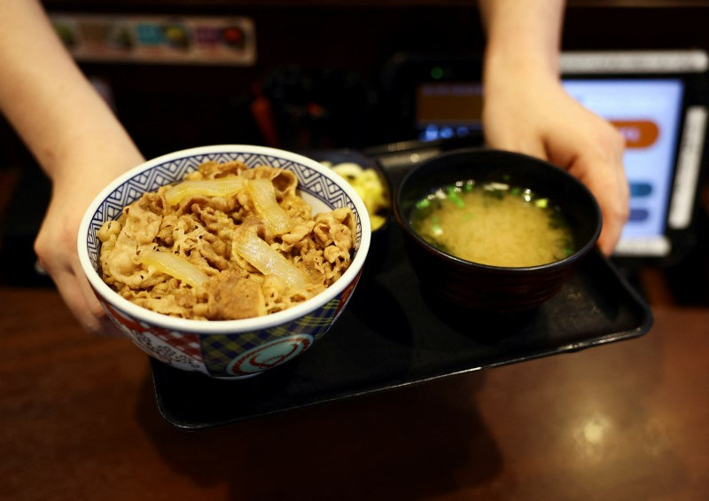 A staff member serves Japanese fast-food 'gyudon' beef bowl with miso soup inside Yoshinoya restaurant in Tokyo, Japan May 19, 2025.  REUTERS/Issei Kato