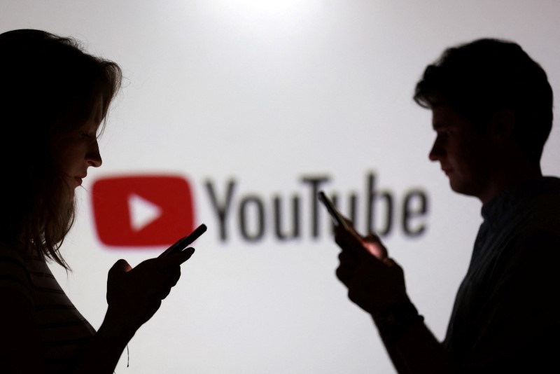 Teenagers pose for a photo while holding smartphones in front of a Youtube logo in this illustration taken September 11, 2025. REUTERS/Dado Ruvic/Illustration