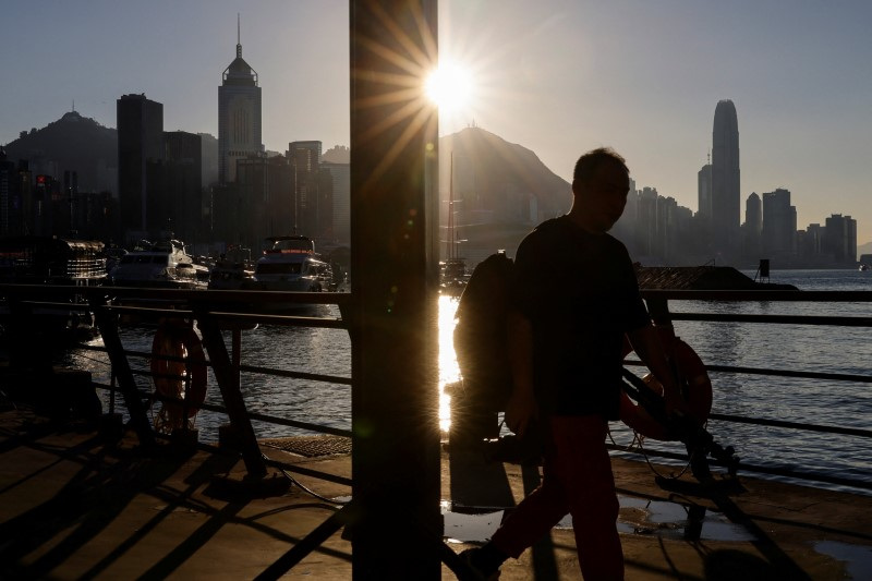 A man walks by the waterfront with skyline buildings across Victoria Harbor in Hong Kong, China October 24, 2023. REUTERS/Tyrone Siu