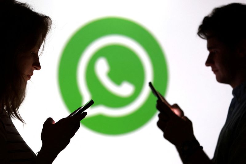 Teenagers pose for a photo while holding smartphones in front of a Whatsapp logo in this illustration taken September 11, 2025. REUTERS/Dado Ruvic/Illustration
