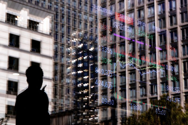 A man walks past a brokerage house, as an electronic board displays stock index information graph, in the Central Business District (CBD) in Beijing, China, October 13, 2025. REUTERS/Maxim Shemetov