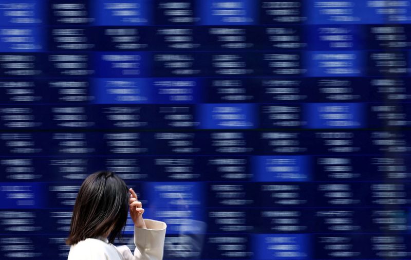A woman walks past an electronic screen displaying stock quotation board in Tokyo, Japan April 15, 2025. REUTERS/Issei Kato