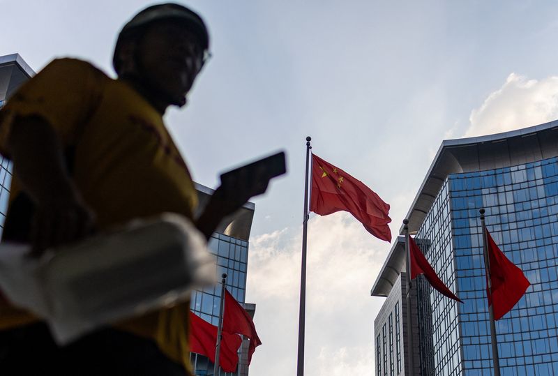 A delivery worker walks next to a Chinese national flag and multiple red flags installed at a courtyard of a business center in Beijing, China, July 8, 2026. REUTERS/Maxim Shemetov