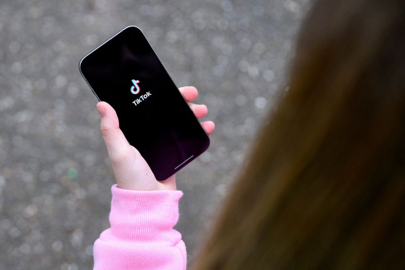 FILE PHOTO: A teenager poses for a picture with a phone displaying the TikTok logo, in Bonn, Germany, February 20, 2026. REUTERS/Jana Rodenbusch/File Photo