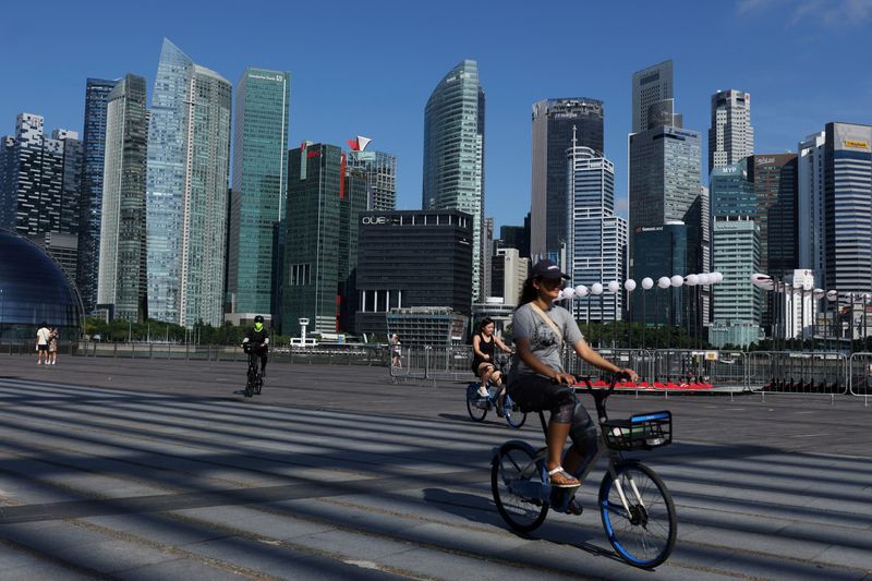 FILE PHOTO: People ride bikes past the skyline of the central business district in Singapore, June 13, 2025. REUTERS/Edgar Su/File Photo