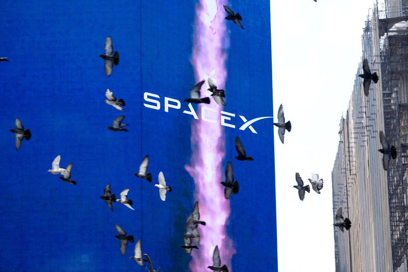 FILE PHOTO: Birds fly past a SpaceX advertisement outside the Nasdaq MarketSite, on the day of SpaceX's initial public offering (IPO), in New York City, U.S., June 12, 2026. REUTERS/David Dee Delgado/ File Photo