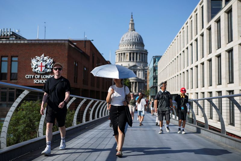A woman uses an umbrella to shield herself from the sun as she walks across Millennium Bridge, with St Paul's Cathedral in the background, during a heatwave in London, Britain, August 13, 2026. REUTERS/Isabel Infantes