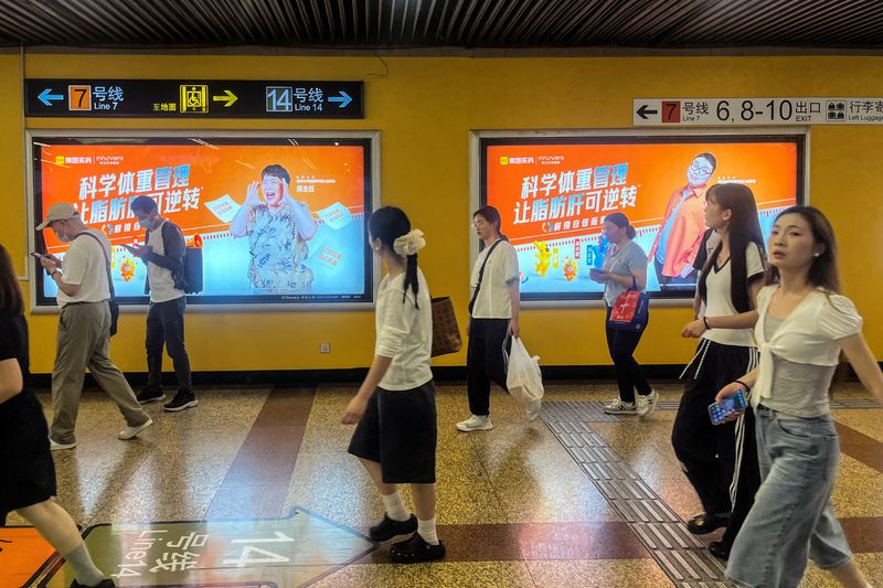 People walk past billboards from Innovent Biologics and Meituan displayed on a wall in a metro station in Shanghai, China July 6, 2026. REUTERS/Andrew Silver