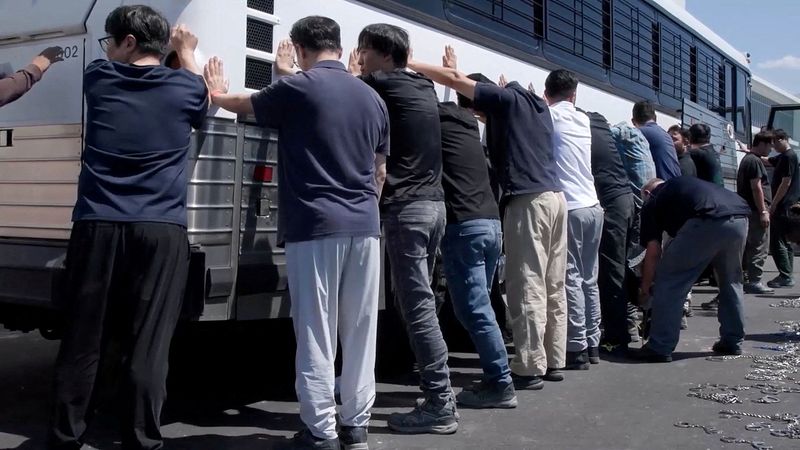 FILE PHOTO: Detainees are made to stand against a bus before being handcuffed, during a raid by federal agents where about 300 South Koreans were among 475 people arrested at the site of a $4.3 billion project by Hyundai Motor and LG Energy Solution to build batteries for electric cars in Ellabell, Georgia, U.S., September 4, 2025 in a still image taken from a video.  U.S. Immigration and Customs Enforcement/Handout via REUTERS/File Photo