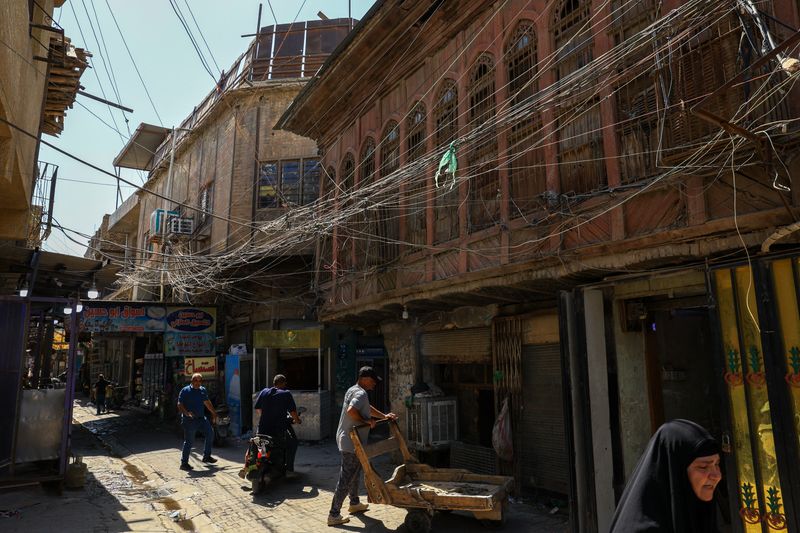 People walk along an old street as a tangled web of electrical wires from a generator supplying homes with electricity hangs above buildings, in Baghdad, Iraq, September 10, 2025. REUTERS/Thaier Al-Sudani
