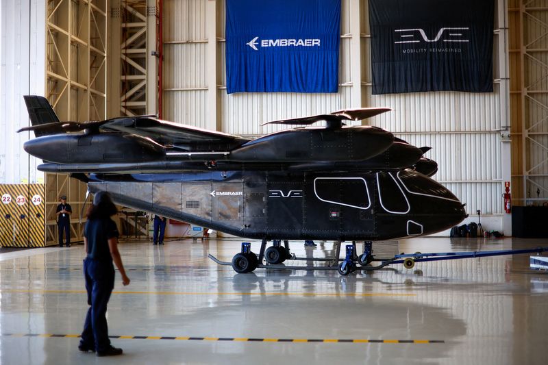 FILE PHOTO: Employees stand near the full-scale prototype of electric vertical take-off and landing (eVTOL) aircraft developed by Eve Air Mobility, an Embraer group company, as it is presented for the first time in Gaviao Peixoto, Brazil July 3, 2024. REUTERS/Amanda Perobelli/File Photo