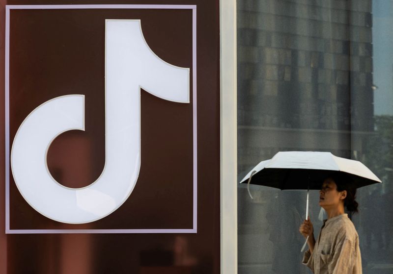 A woman walks past a logo of Tik Tok social network on Wangfujing street in Beijing, China August 7, 2025. REUTERS/Maxim Shemetov