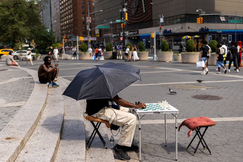 FILE PHOTO: A man holds an umbrella while playing chess during a heatwave affecting the U.S. Northeast in New York City, U.S., June 23, 2024. REUTERS/Jeenah Moon/File Photo