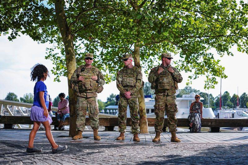 A child walks past members of the National Guard after U.S. President Donald Trump deployed the National Guard and ordered an increased presence of federal law enforcement to assist in crime prevention, in Washington, D.C., U.S., August 23, 2025. REUTERS/Aaron Schwartz