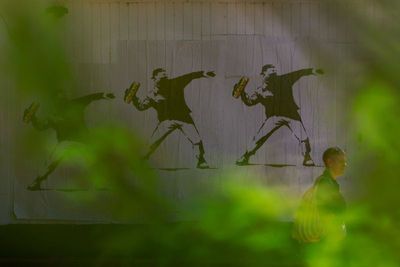 FILE PHOTO: A person walks past signs depicting a man throwing a sandwich, used as a symbol of protest, after U.S. President Donald Trump deployed the National Guard and ordered an increased presence of federal law enforcement to assist in crime prevention, in the Capitol Hill neighborhood, in Washington, D.C., U.S., August 23, 2025. REUTERS/Jose Luis Gonzalez/File Photo
