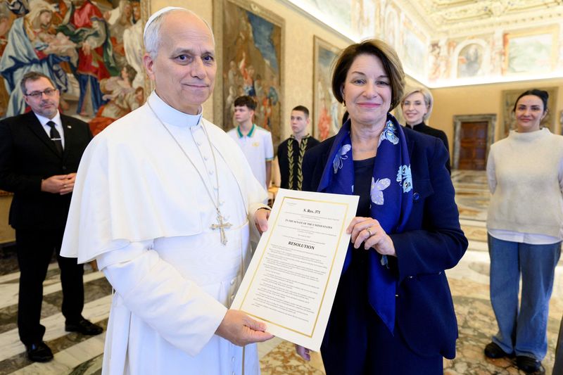 Pope Leo XIV and U.S. Senator Amy Klobuchar (D-MN) pose for a photo with a copy of a U.S. Senate bill commemorating the victims of the shooting at a Minnesota Catholic church and school, at the Vatican, November 21, 2025. Simone Risoluti/Vatican Media/­Handout via REUTERS