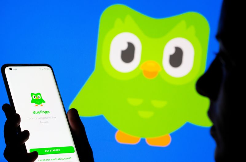 Woman with her smartphone poses in front of displayed Duolingo logo in this illustration taken, June 29, 2021. REUTERS/Dado Ruvic/Illustration/File Photo