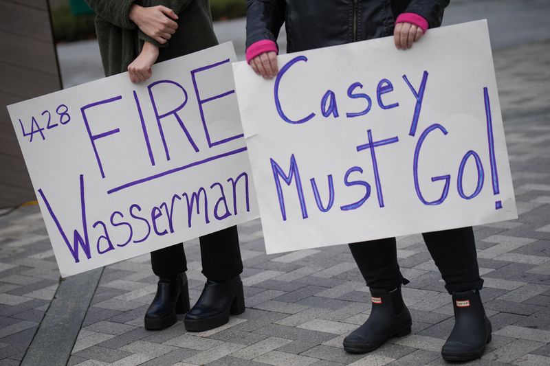People hold placards on the day local elected officials, survivors and activists hold a press conference calling for the removal of Casey Wasserman as head of the LA Olympic Committee following revelations of his ties to Ghislaine Maxwell, in Los Angeles, California, U.S., February 17, 2026. REUTERS/Daniel Cole