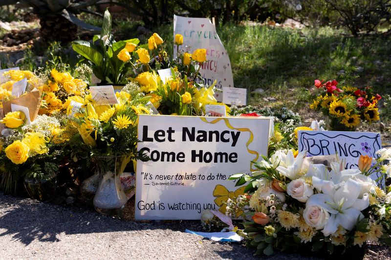 FILE PHOTO: A sign reads stands amid yellow flowers left at the house of Nancy Guthrie, the 84-year-old mother of U.S. journalist and television host Savannah Guthrie, who went missing from her home on February 1, in Tucson, U.S., February 21, 2026.  REUTERS/Rebecca Noble/File Photo