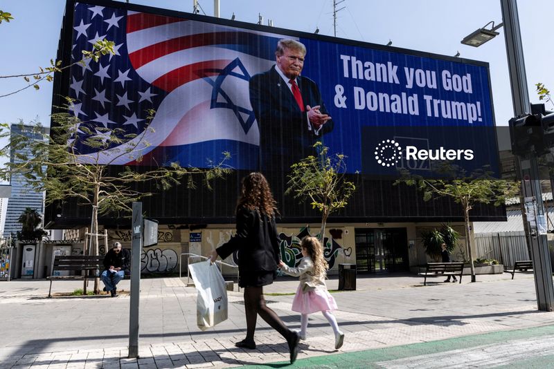 FILE PHOTO: People walk by a billboard commissioned by an evangelical group, which displays a picture of U.S. President Donald Trump with the words "Thank you God & Donald Trump", amid the U.S.-Israel conflict with Iran, in Tel Aviv, Israel, March 12, 2026. REUTERS/Nir Elias/File Photo