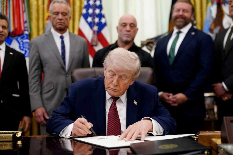 FILE PHOTO: U.S. President Donald Trump signs an executive order encouraging more research into ibogaine, next to U.S. Health and Human Services (HHS) Secretary Robert F. Kennedy Jr., Joe Rogan, and Americans for Ibogaine CEO W. Bryan Hubbard, in the Oval Office of the White House in Washington, D.C., April 18, 2026. REUTERS/Nathan Howard/File Photo