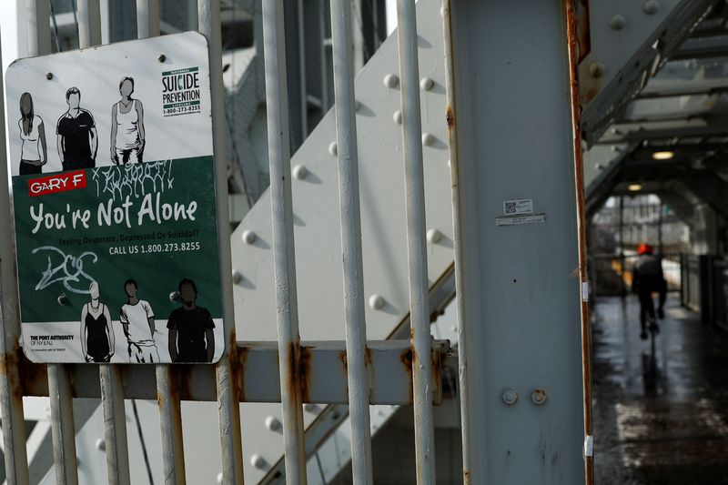 A cyclist rides past a suicide prevention sign on a protective fence on the walkway of the George Washington Bridge between New York and New Jersey in New York, U.S., January 12, 2022. REUTERS/Mike Segar