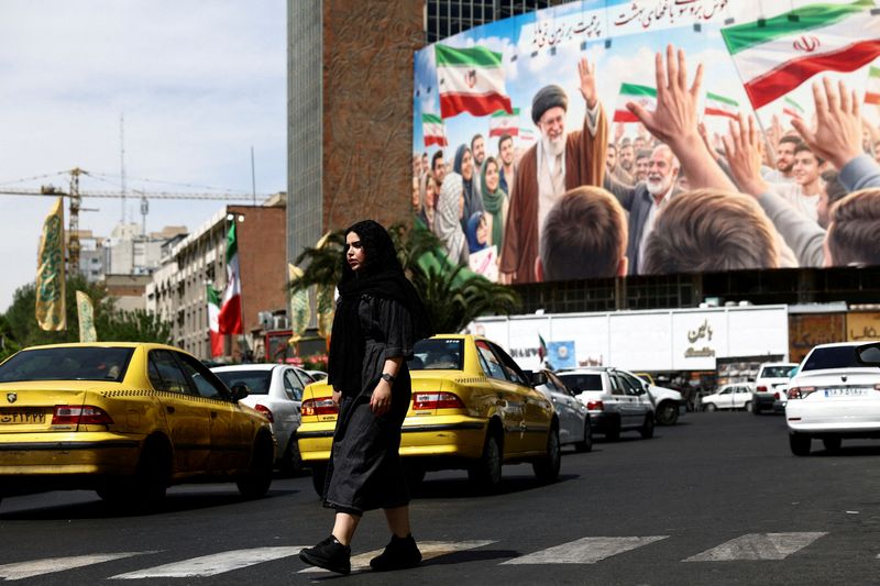 FILE PHOTO: A woman walks past a billboard featuring an image of the late Supreme Leader of Iran, Ayatollah Ali Khamenei, on a building, amid a ceasefire between U.S. and Iran, in Tehran, Iran, April 27, 2026. Majid Asgaripour/WANA (West Asia News Agency) via REUTERS/File Photo