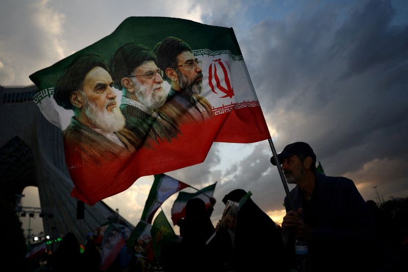 FILE PHOTO: A man holds a flag with a picture of late leader of the Islamic Revolution Ayatollah Ruhollah Khomeini, late Supreme Leader of Iran Ayatollah Ali Khamenei and Iran's new Supreme Leader Mojtaba Khamenei, during a rally in Tehran, Iran, April 29, 2026. Majid Asgaripour/WANA (West Asia News Agency) via REUTERS/File Photo