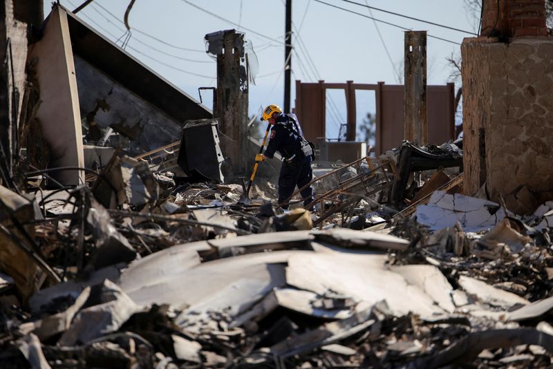 A search and rescue worker investigates the charred remains of a house, as the Eaton Fire continues, in Altadena, Los Angeles County, California, U.S. January 15, 2025. REUTERS/Daniel Cole