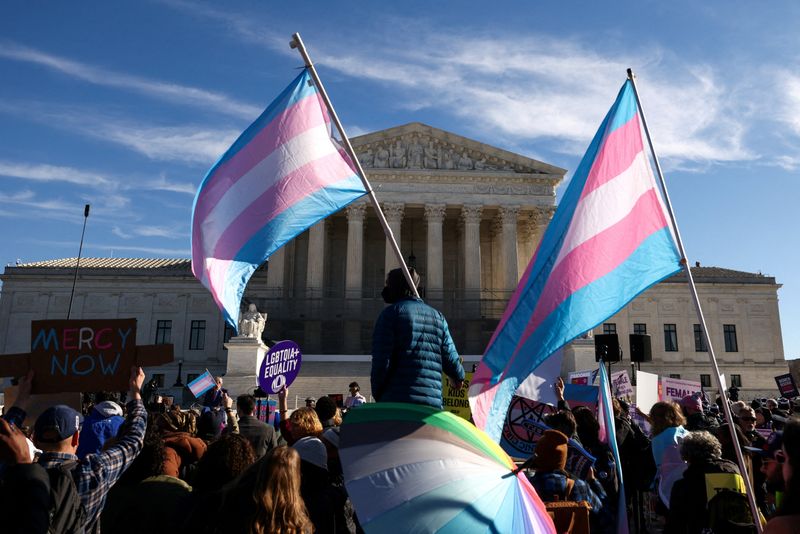 FILE PHOTO: Demonstrators carry a transgender flags outside the U.S. Supreme Court, on the day the justices heard oral arguments in two cases concerning efforts to enforce Republican-backed state laws banning transgender athletes from female sports teams at public schools, in Washington, D.C., U.S., January 13, 2026. REUTERS/Kevin Lamarque/File Photo