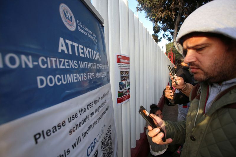 Migrants check their phones while gathering at El Chaparral border crossing after their CBP One app asylum appointment was cancelled on the day of U.S. President Donald Trump's inauguration, in Tijuana, Mexico January 20, 2025. REUTERS/Jorge Duenes
