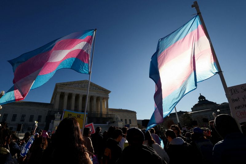 FILE PHOTO: Demonstrators carry a transgender flags outside the U.S. Supreme Court, on the day justices are expected to hear oral arguments in two cases concerning efforts to enforce Republican-backed state laws banning transgender athletes from female sports teams at public schools, in Washington, D.C., U.S., January 13, 2026. REUTERS/Kevin Lamarque/File Photo