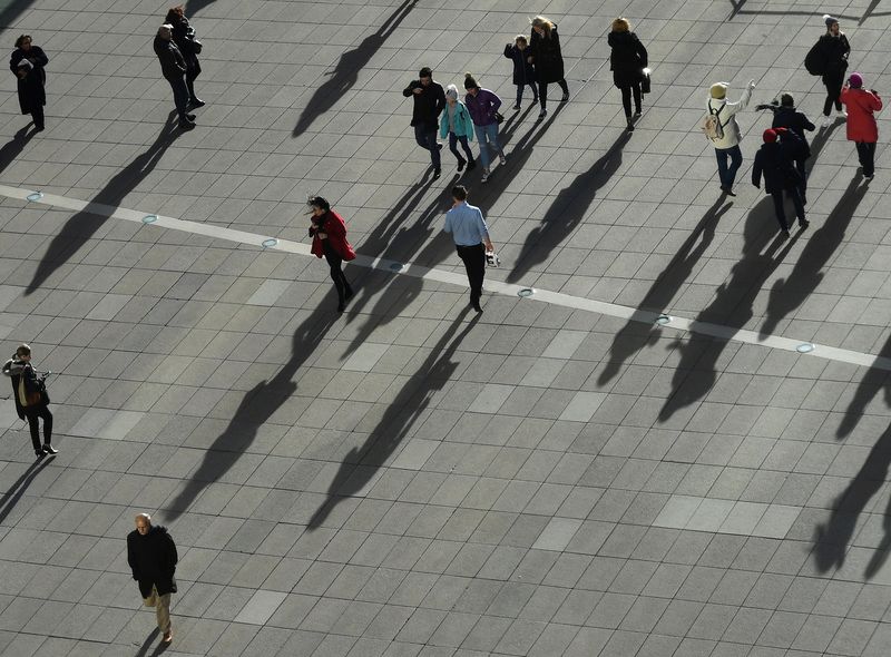 FILE PHOTO: People cast long shadows in the winter sunlight as they walk across a plaza in the Canary Wharf financial district of London, Britain, January 17, 2018. REUTERS/Dylan Martinez/File Photo