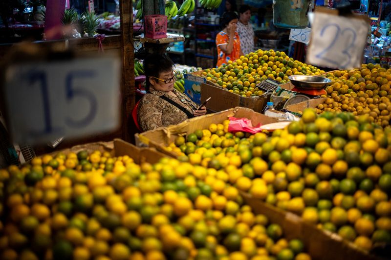 FILE PHOTO: A vendor looks at a mobile phone at her fruit stall at a market in Bangkok, Thailand, October 2, 2023. REUTERS/Athit Perawongmetha/ File Photo