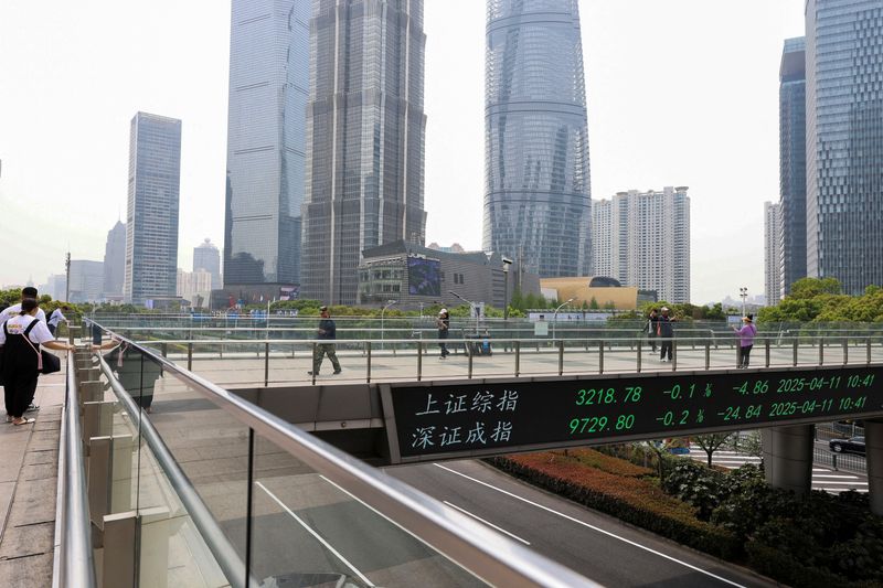 FILE PHOTO: An electronic board shows Shanghai and Shenzhen stock indices as people walk on a pedestrian bridge at the Lujiazui financial district in Shanghai, China April 11, 2025. REUTERS/Go Nakamura/File Photo