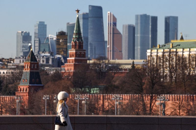 FILE PHOTO: A woman walks along a bridge, with the Moscow City business centre and the Kremlin wall seen in the background, on a sunny day in Moscow, Russia, February 24, 2025. REUTERS/Evgenia Novozhenina/File Photo