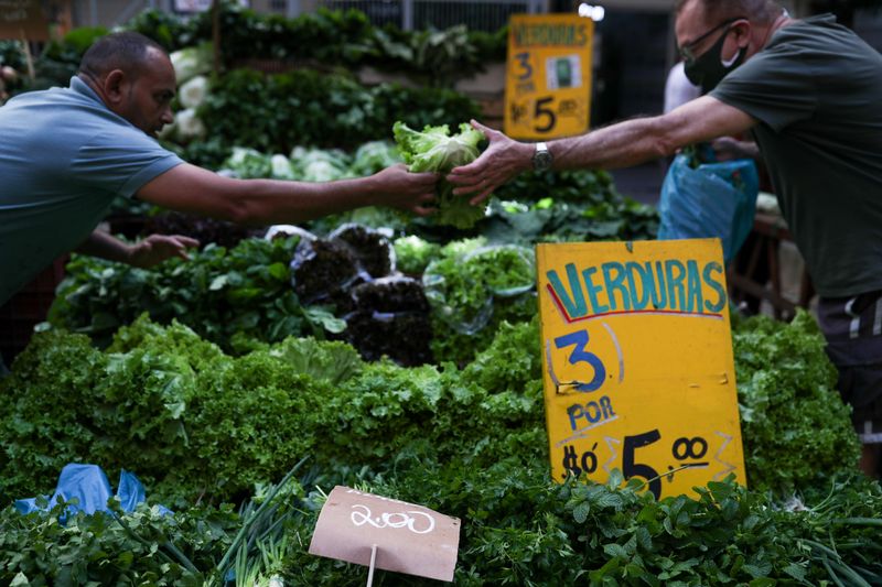 FILE PHOTO: A man hands over a lettuce to another man as prices are displayed at a weekly street market in Rio de Janeiro, Brazil July 8, 2021. REUTERS/Amanda Perobelli/File Photo