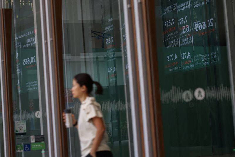 FILE PHOTO: A screen reflecting on glass displays the Hang Seng stock index at the Central district in Hong Kong, China, April 7, 2025. REUTERS/Tyrone Siu/ File Photo