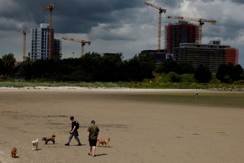 FILE PHOTO: People walk their dogs on Sandymount beach as construction cranes are visible on new high rise buildings in the distance, in Dublin, Ireland, July 2 2025. REUTERS/Clodagh Kilcoyne/File Photo