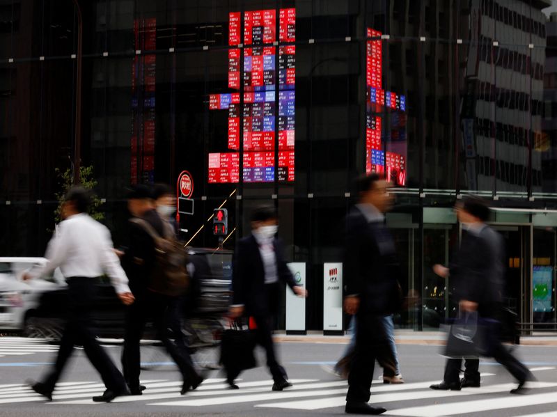 Pedestrians walk past an electronic board displaying various companies' share prices, at a business district in Tokyo, Japan, October 31, 2023. REUTERS/Kim Kyung-Hoon