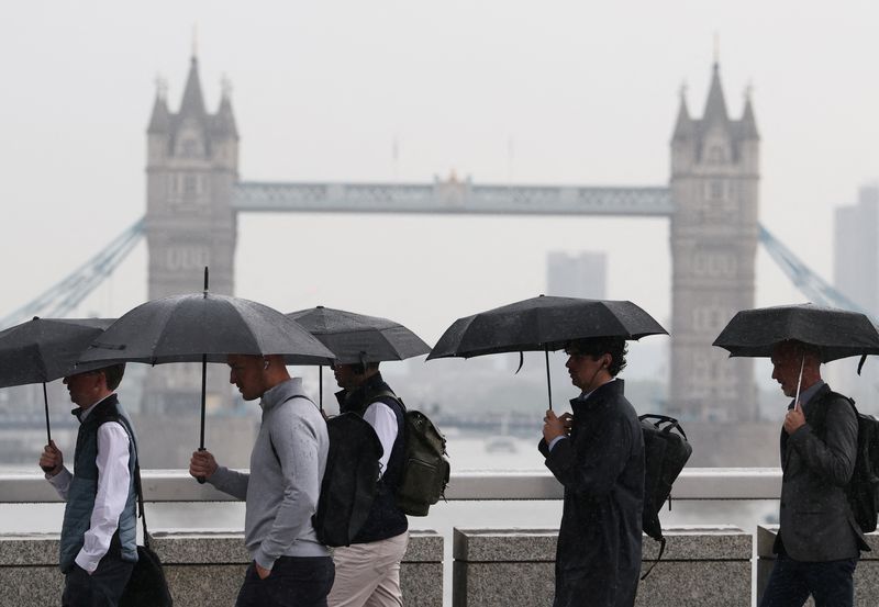 Workers shield from the rain as they cross London Bridge during the morning rush-hour, with Tower Bridge seen behind, in London, Britain, May 21, 2025. REUTERS/Toby Melville/File Photo