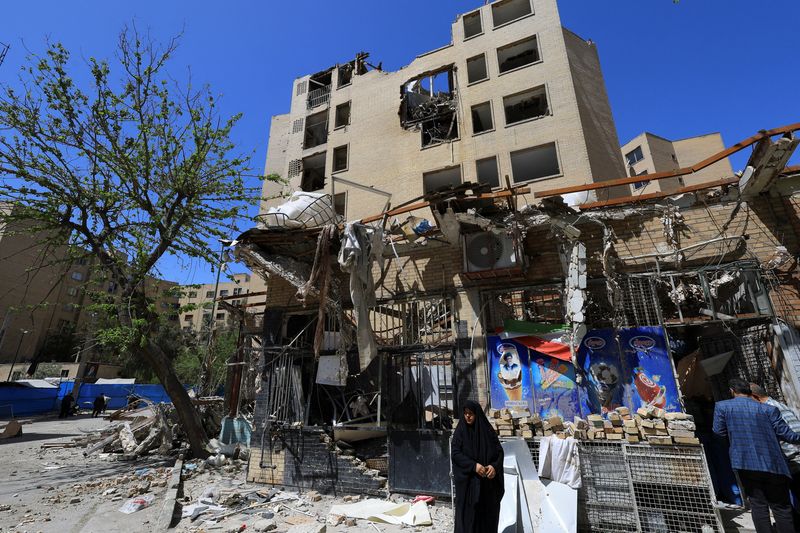 A woman stands next to debris lying in front of a residential building damaged by a strike on March 4, in Tehran, Iran, April 14, 2026. REUTERS/Thaier Al Sudani